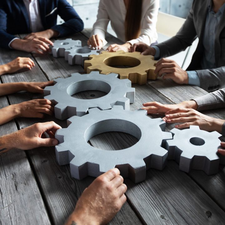 Group of business people joining together silver and golden colored gears on table at workplace